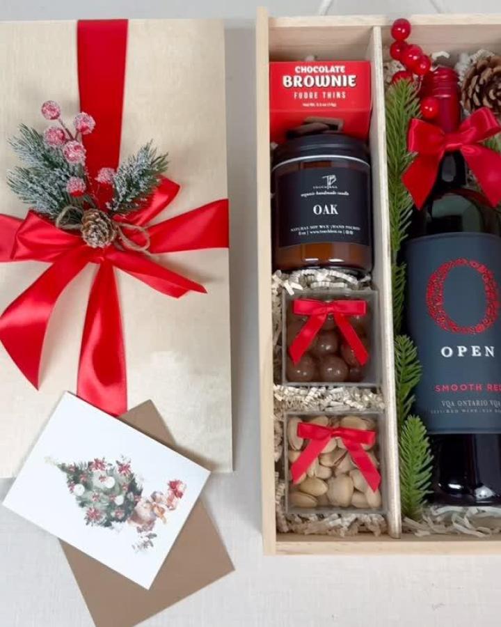 Wooden gift box from @touch_box filled with gourmet treats, wine, and festive red ribbon decorations.