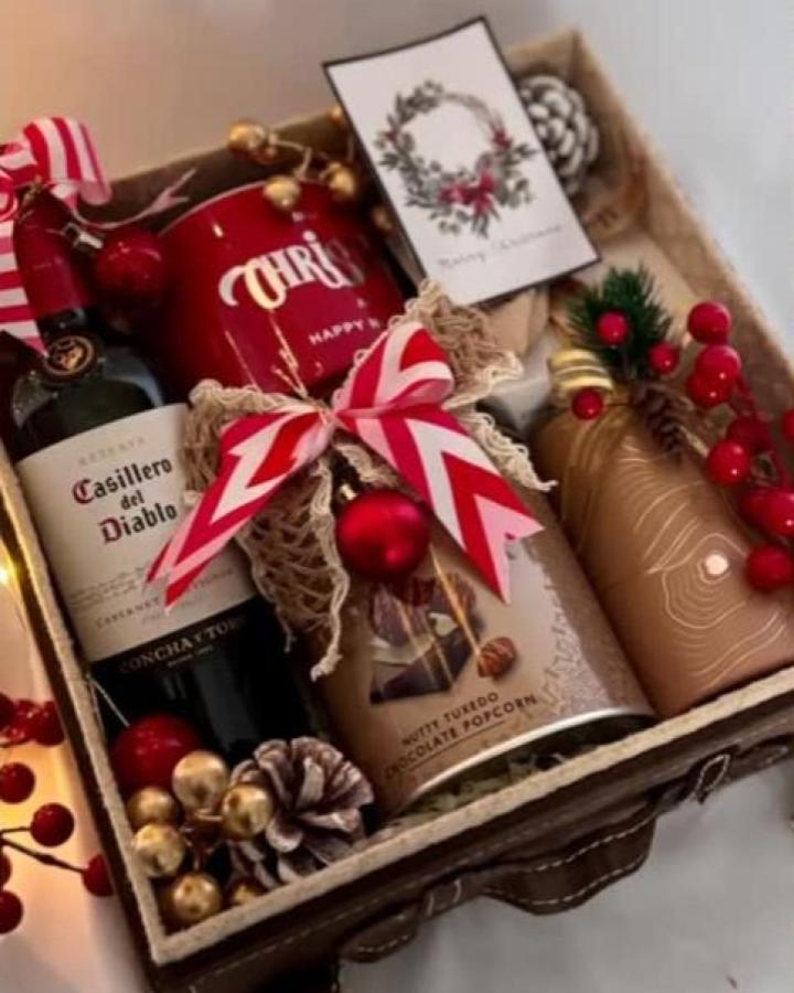 Festive woven basket from @giftalittledubai with ribbon-wrapped wine, ornaments, and holiday treats inside.