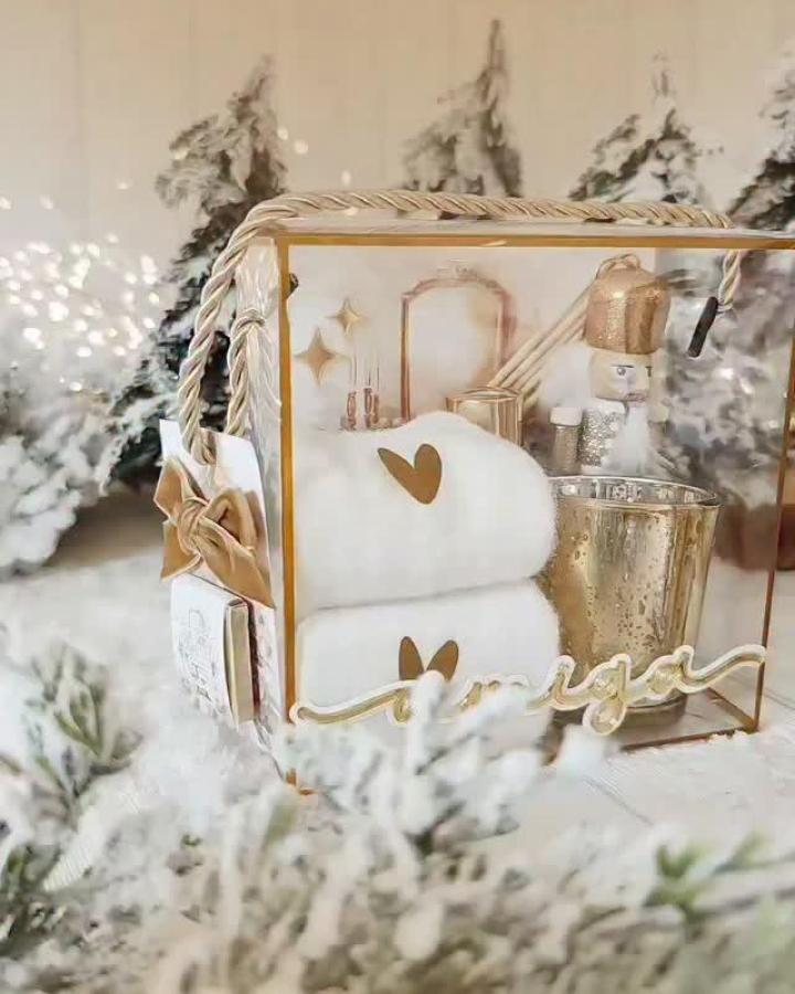Gold-trimmed glass display box from @_little_parties featuring white spa towels and festive holiday decorations.