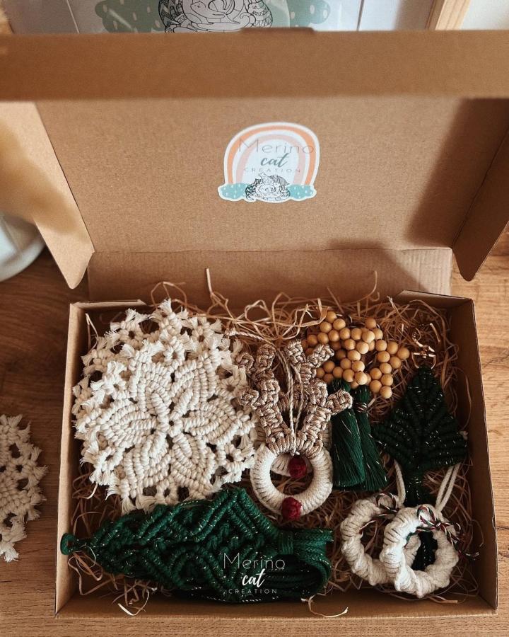 Handmade macrame ornament collection from @merinocatcreation in kraft box with cream snowflake and green tassels.