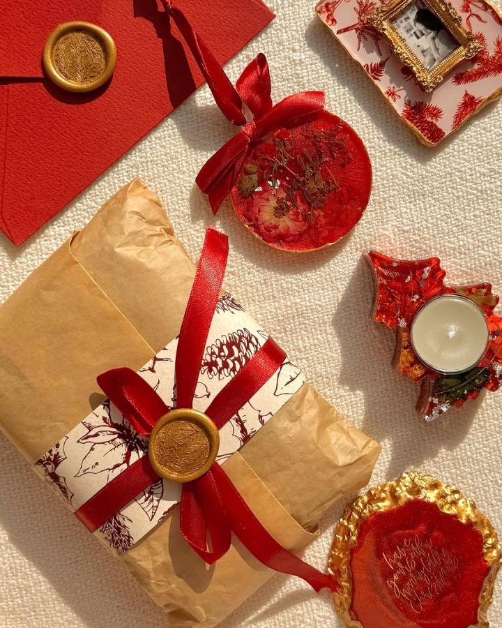 Red resin ornaments and kraft paper gifts from @the_tinted_palette with gold wax seal details and satin ribbons.