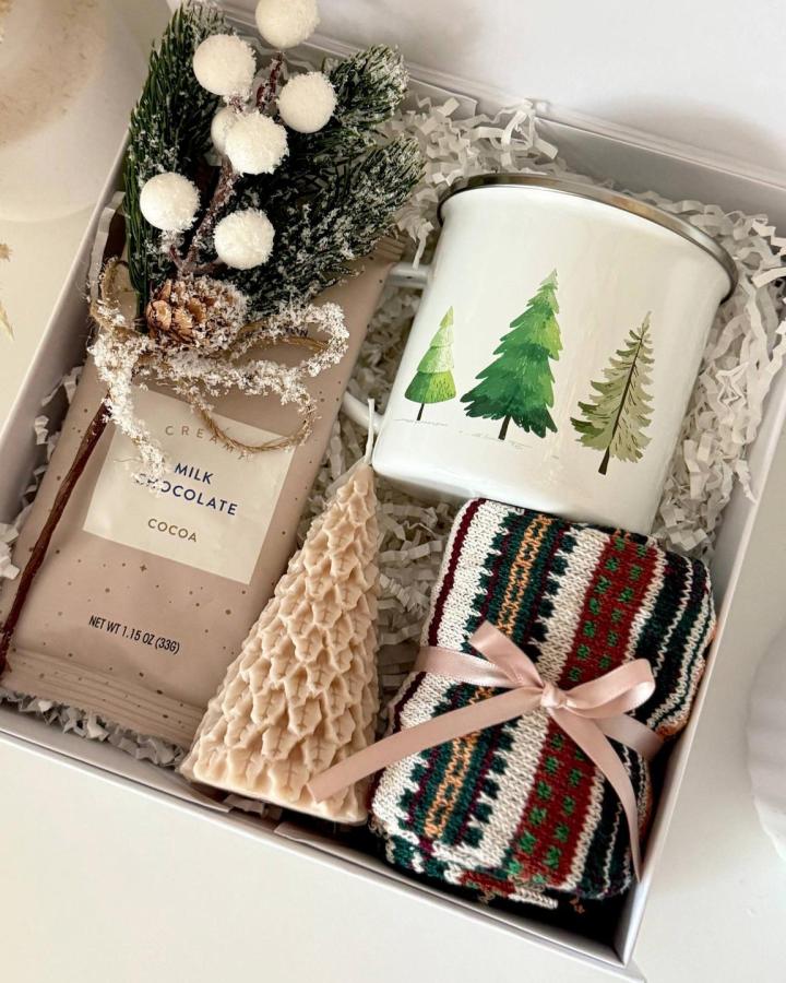 Winter-themed gift box from @cuteboxesboutique with evergreen mug, cocoa, and knit throw tied with ribbon.