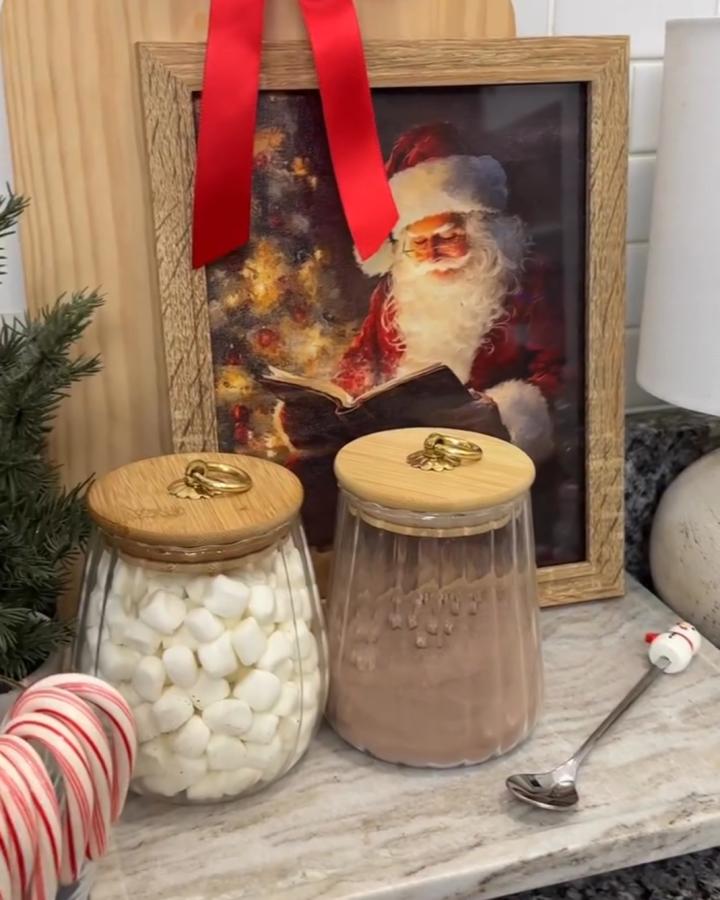 Framed Santa artwork and glass jars from @jojos_home_decor. Marble tray with candy canes and cocoa toppings.