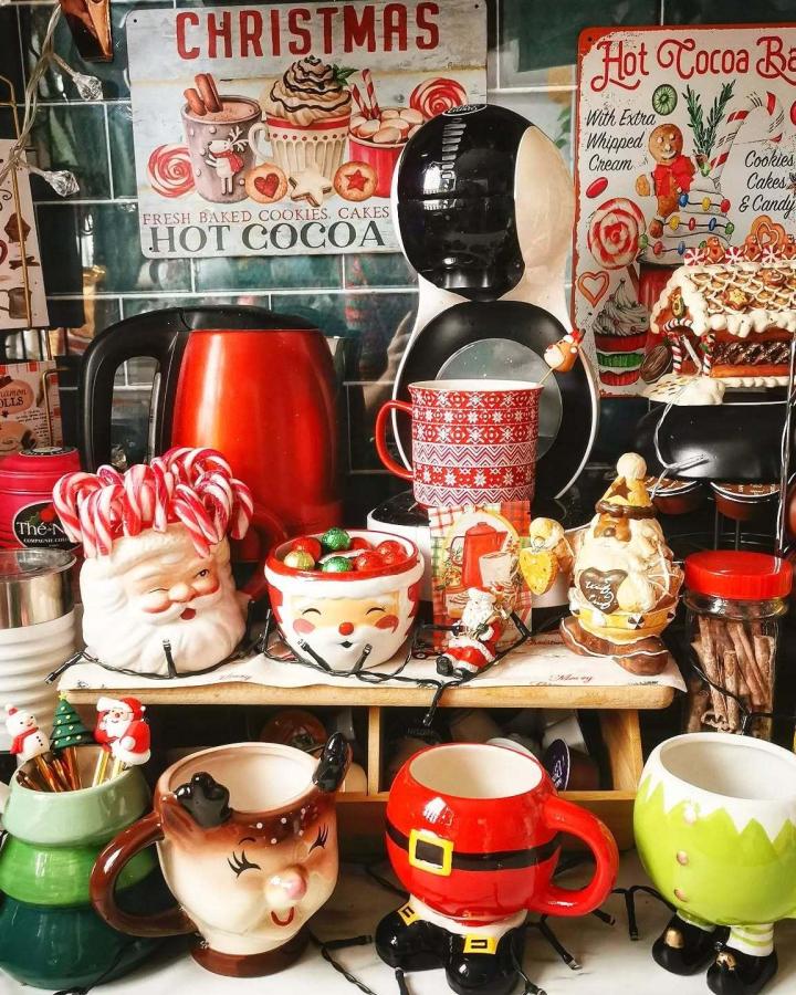Ceramic character mugs displayed on wooden shelves from @marjoaime featuring Santa, reindeer, and elf designs.