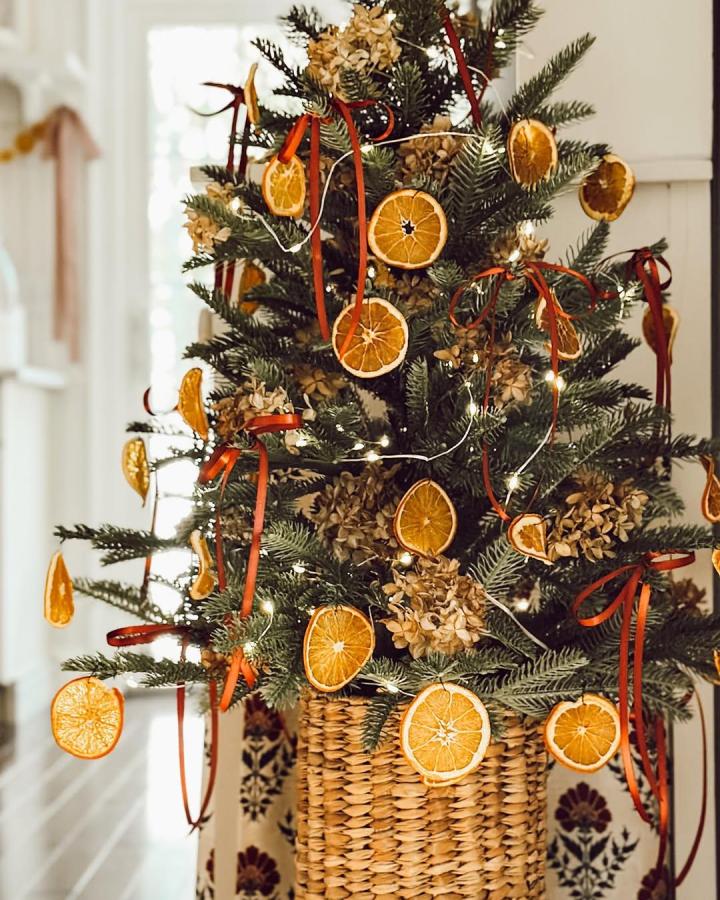Festive tree decorated with dried orange slices and velvet ribbons from @eleanorrosehome in woven basket base