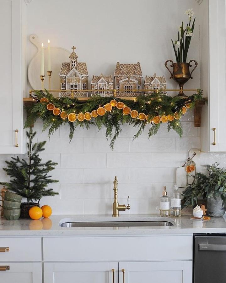Kitchen shelf styling from @dearlillie featuring dried orange garland draped over evergreen branches with gingerbread houses.
