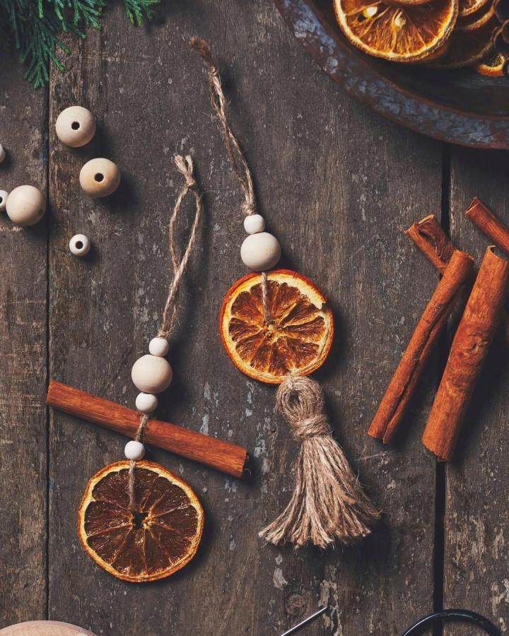 Rustic garland craft from @sostrenegrene featuring dried orange slices, wooden beads, and cinnamon sticks on twine.