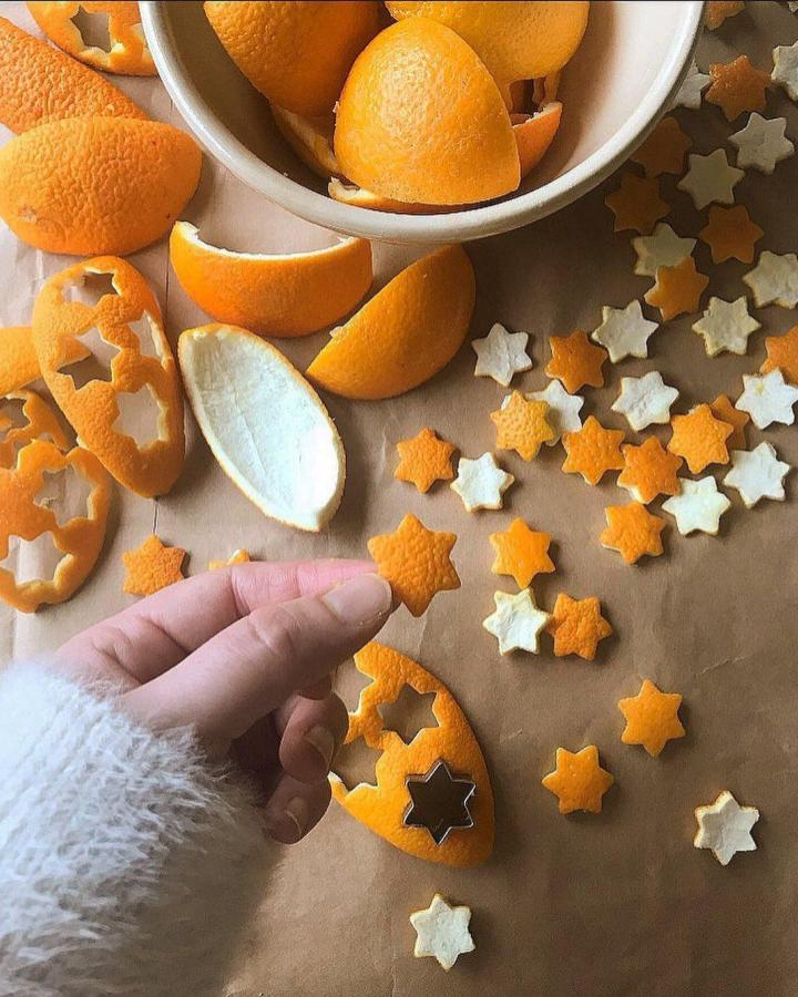 Bright orange and cream star-shaped peel cutouts from @uselessplastic scattered across parchment paper with whole oranges.