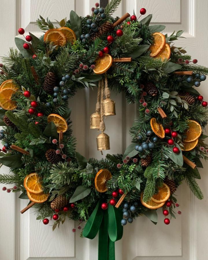 Festive wreath featuring diy dried orange christmas decorations from @sentimentaldecor with berries and pine branches.