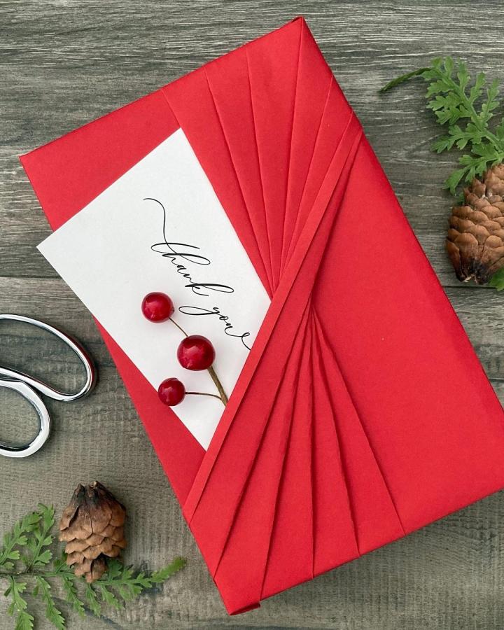 Red pleated paper wrap from @giftwrappinglove featuring elegant christmas gift wrapping ideas with calligraphy tag and berry accents.