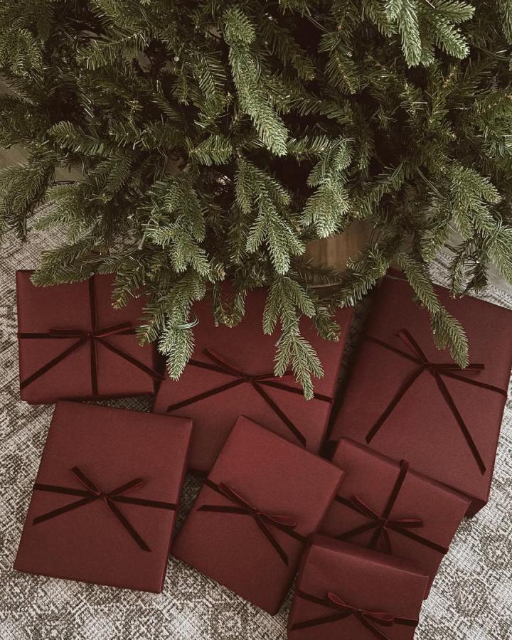 Burgundy wrapped gifts from @jensgatheringnest with brown velvet ribbon beneath evergreen branches.
