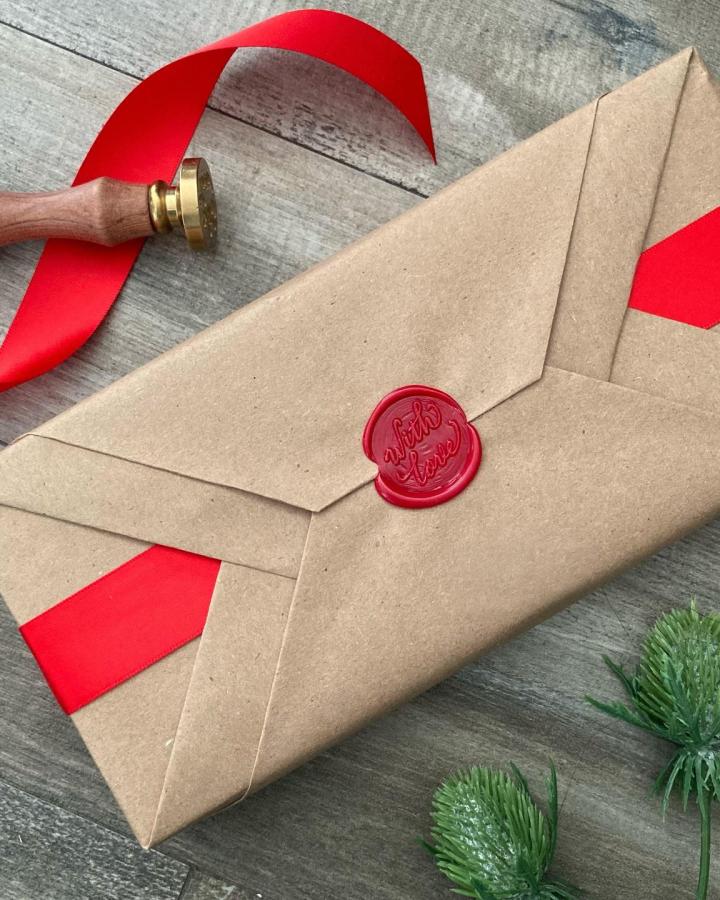 Red wax seal on kraft paper gift wrap from @giftwrappinglove featuring brass stamp and ribbon.