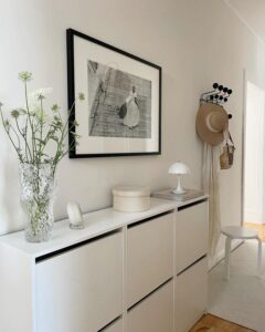 White minimalist Ikea Bissa shoe cabinet in neutral hallway with natural decor and black photo frame from @parkplaceabode. Cozy and tidy ikea bissa hacks & ideas.