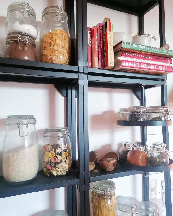 Black metal Ikea Enhet shelving with glass jars and cookbooks from @at.home.with.the.moseys. Kitchen storage and decor.