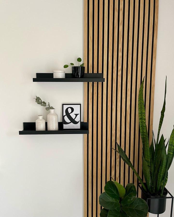 Black floating shelves from @liebes_zuhause_ styled with ikea mosslanda hacks & ideas and wooden slat backdrop.