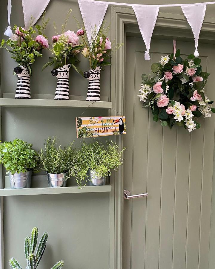Sage green shelves with striped zebra vases from @fe.foreverhome. Pink florals and summer bunting complete the porch display.