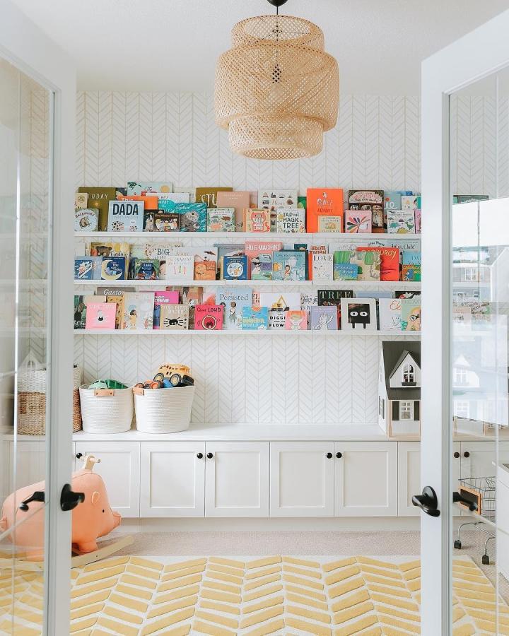 White picture ledges from @ikea_australia. Stacked shelving displays colorful children's books face-out in bright playroom.