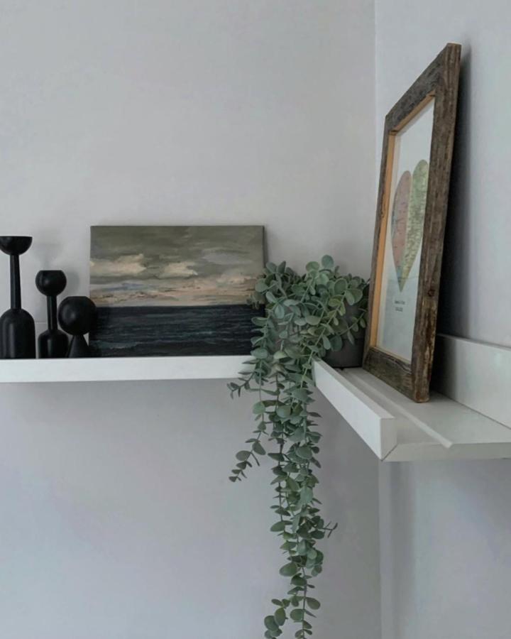White layered picture ledge display from @thathomelife_. Eucalyptus trails between framed art and mirror.