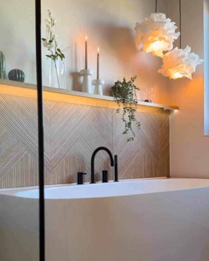 Illuminated wooden ledge shelf from @homeheartmade above white bathtub with decorative candles and greenery.