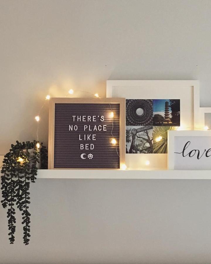 White shelf with fairy lights and letter board from @helenmclean.curated. Trailing plant adds texture.