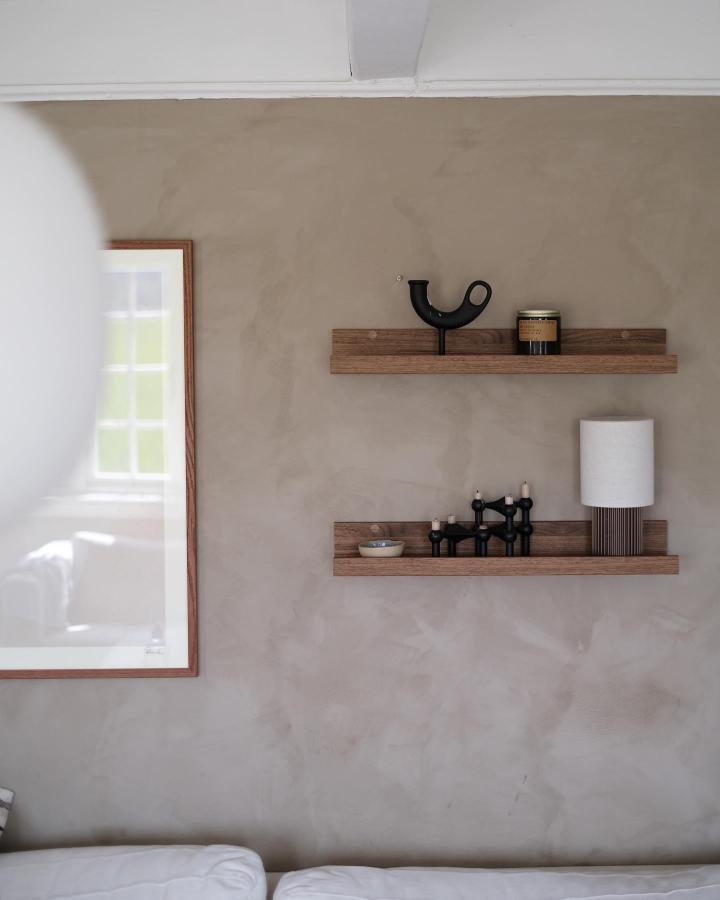 Walnut-stained floating shelves from @miriamskrovje. Minimalist bedroom styling with black decorative objects.