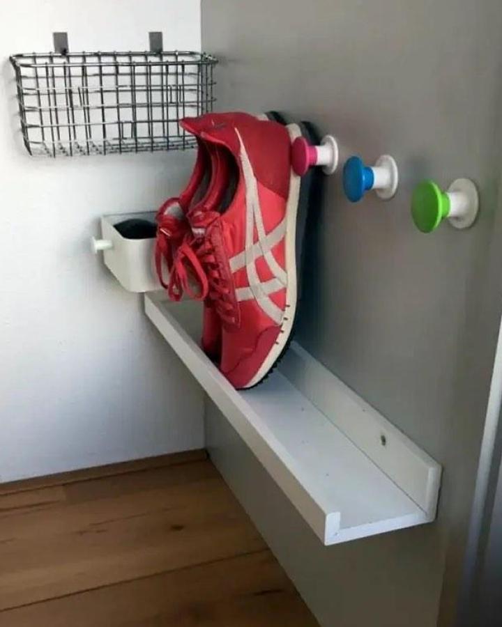 White Mosslanda shoe ledge from @ikeahackersofficial. Colorful hooks and wire basket complete the entryway setup.
