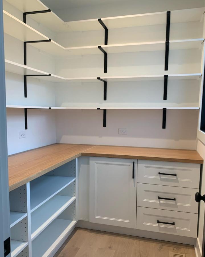 Minimal white pantry shelving with black brackets from @dealsformomsblog. Bright built-in shelves above wood countertop and drawers.
