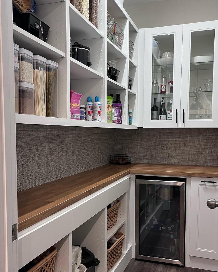 White built-in pantry shelving from @appleonadime. Clear containers, woven baskets, and wood counter with glass cabinets.
