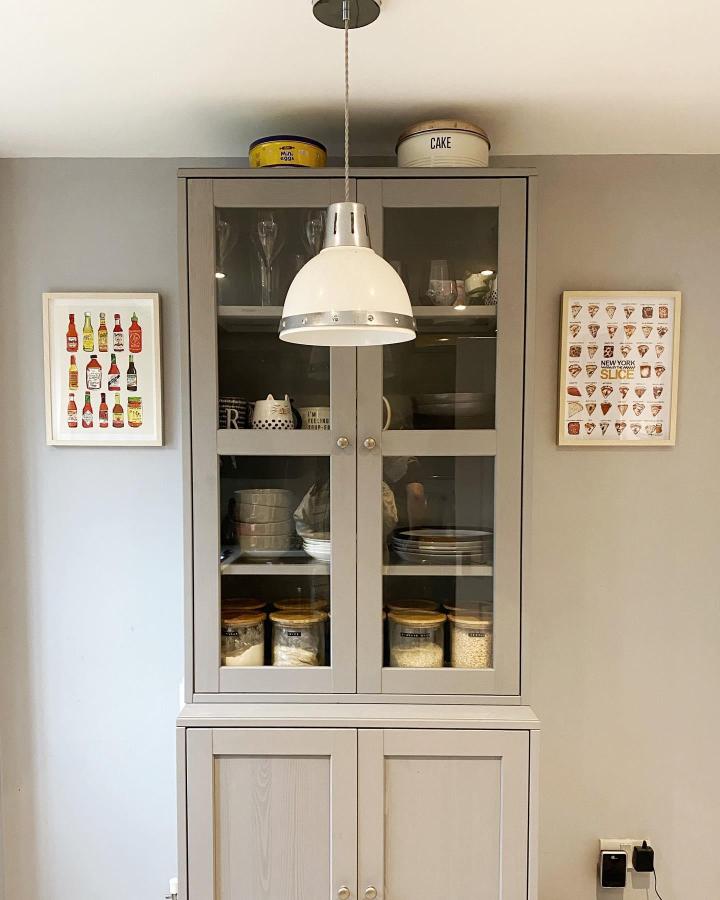 Soft gray glass-door cupboard pantry from @riaathome. Clear jars and stacked dishes for organized dry goods.