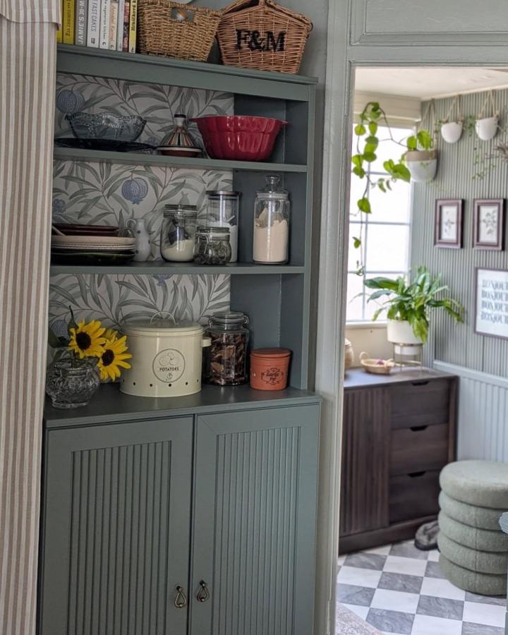 Soft blue-green built-in pantry shelving from @housetohomebyaneta. Wicker baskets, glass jars, and beadboard cabinet doors.