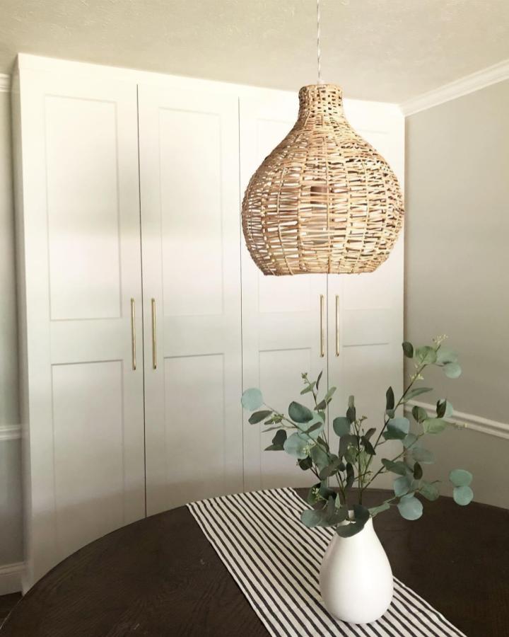 Crisp white Shaker cabinet pantry wall from @anne.curwen. Brass bar pulls and woven rattan pendant styling.