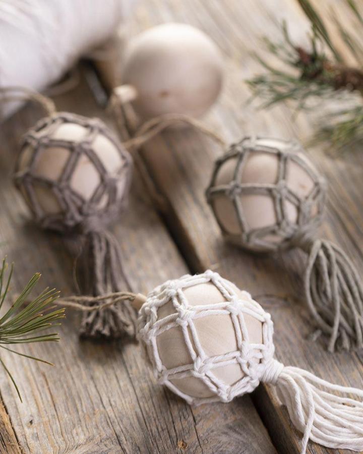 Natural netted macrame christmas ornament ideas from CC Craft featuring wooden beads and cream tassels on rustic wood surface.