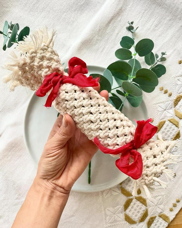 Cream macrame candy ornament with red ribbon from @_twome held against eucalyptus backdrop