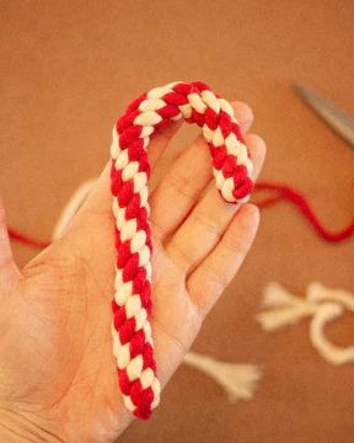 Red and white braided candy cane ornament from @_twome held in hand showing striped pattern detail.