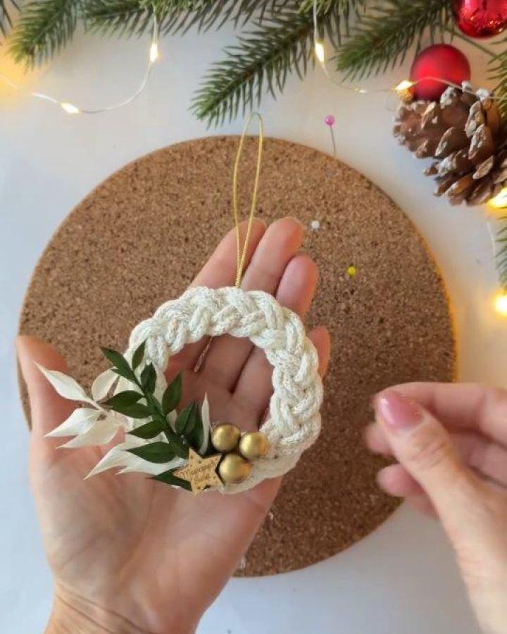 Cream braided wreath ornament from Creataholic with greenery and gold bells held in hand.