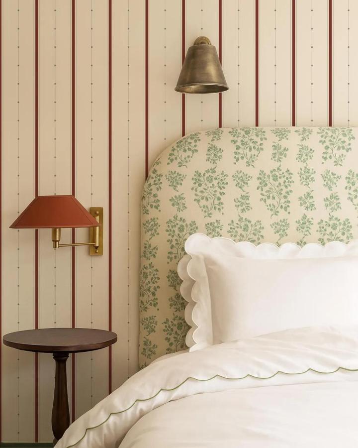 Cream and russet red striped wallpaper in cozy bedroom from PatternHueShop with floral headboard and scalloped bedding.
