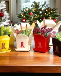 Yellow red black takeout box succulent planter ideas from Marbol3DWorkshop arranged on wooden table near holiday tree lights.