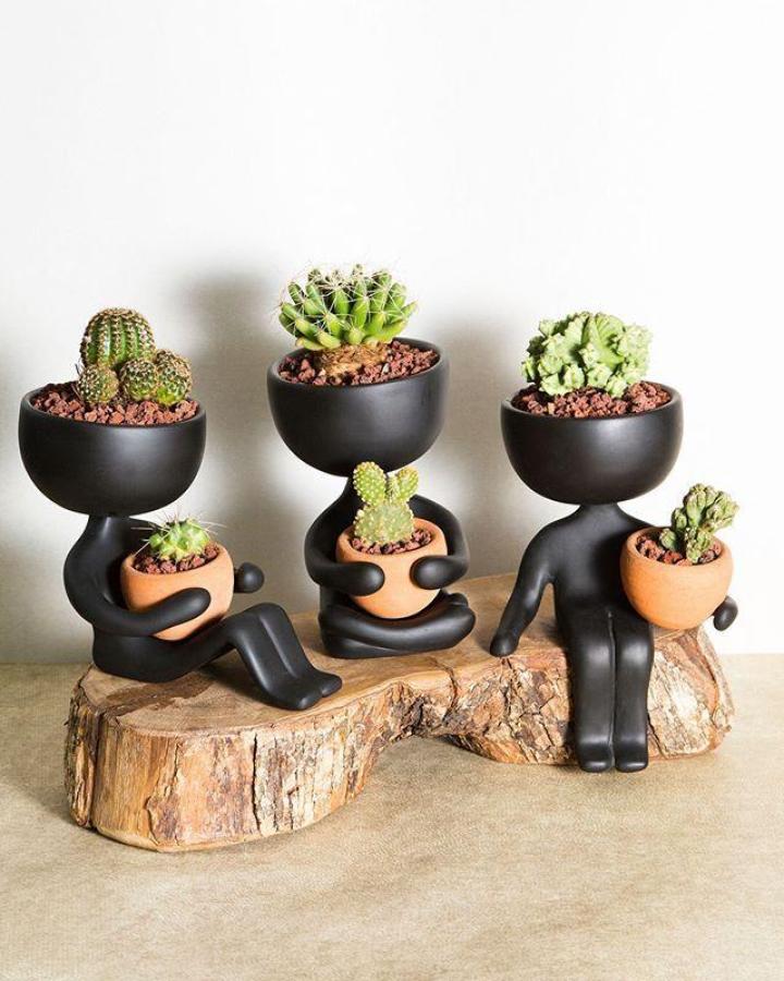 Black matte figurine planters with terracotta pots on a rustic wood slab from Estudio Floga featuring playful succulent planter ideas.