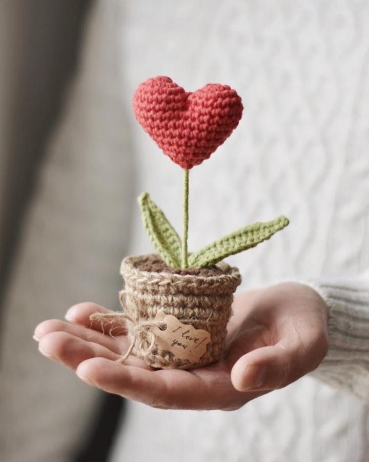 Soft red and green yarn crochet flower in a brown textured pot from @fireflycrochets crochet valentines ideas with a handwritten tag.