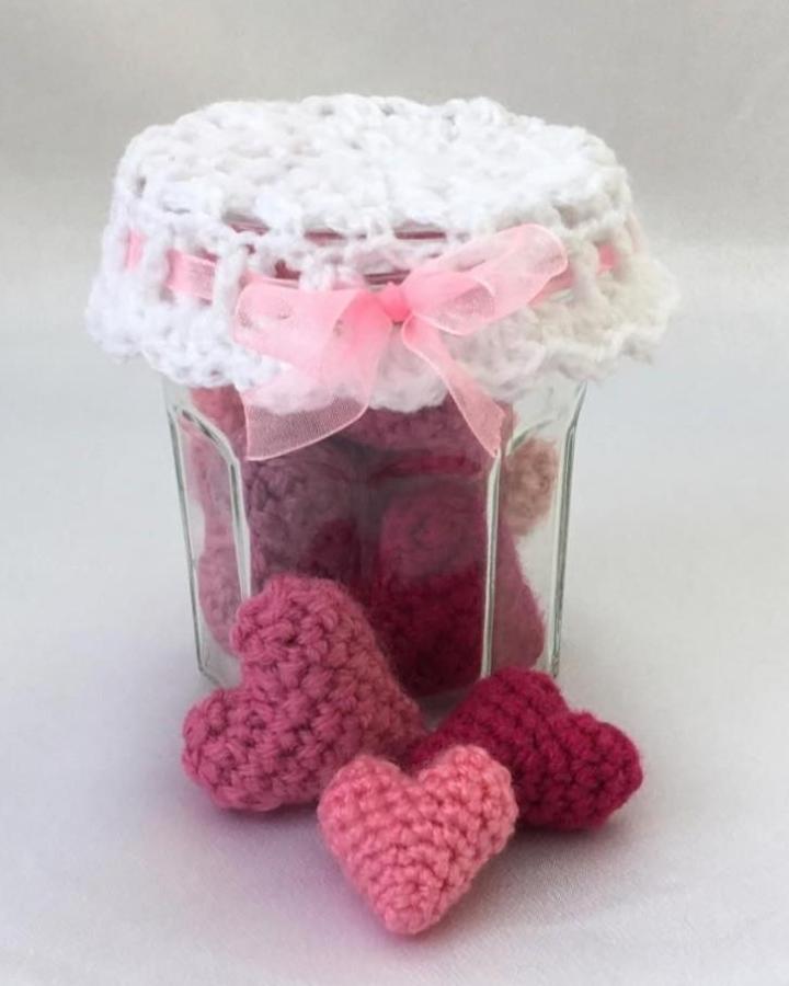 Pink and rose crochet hearts in a glass jar with a white crocheted lid and pink ribbon from @hookedonpatterns for crochet valentines ideas.