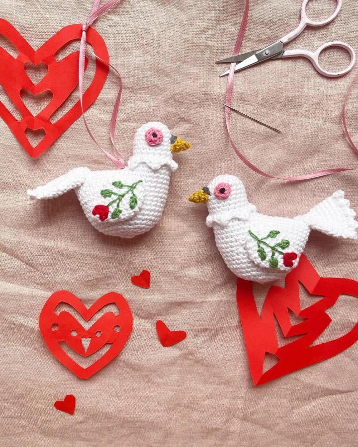 White crocheted love birds with embroidered red berries and yellow beaks on linen fabric from @frau_apfelkern with scissors and ribbon.