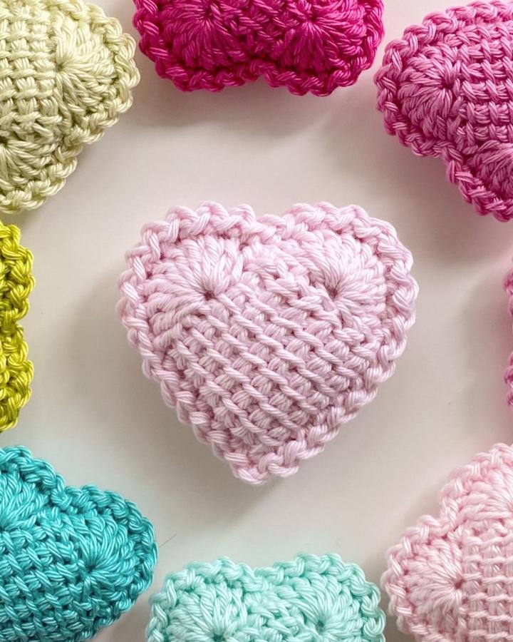 Pink chunky crocheted heart with soft stitch texture surrounded by colorful crochet hearts from @crochetroad crochet valentines ideas plush handcrafts.