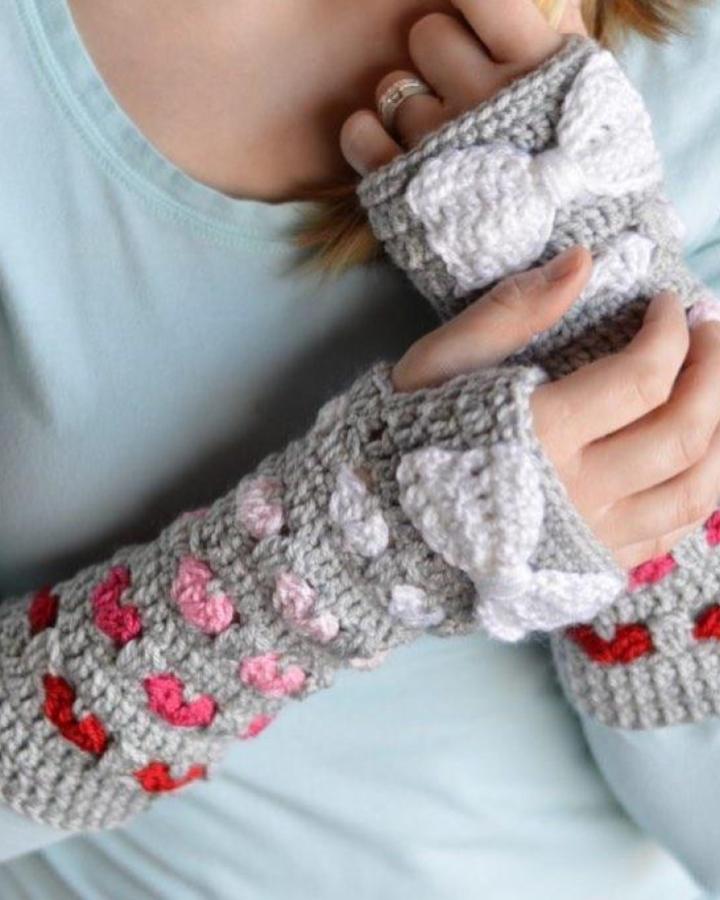 Grey wrist warmers with pink and red hearts and white crochet bows from @whistleandivy showing crochet valentines ideas.