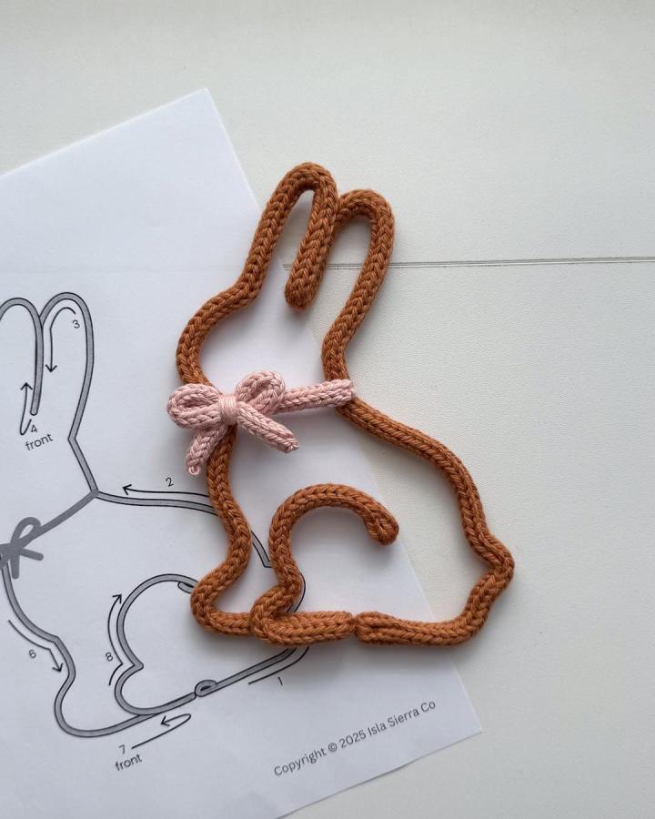 Brown knitted bunny outline with pink bow from @isla.sierra_co. Easter bunny crafts for adults with pattern guide.