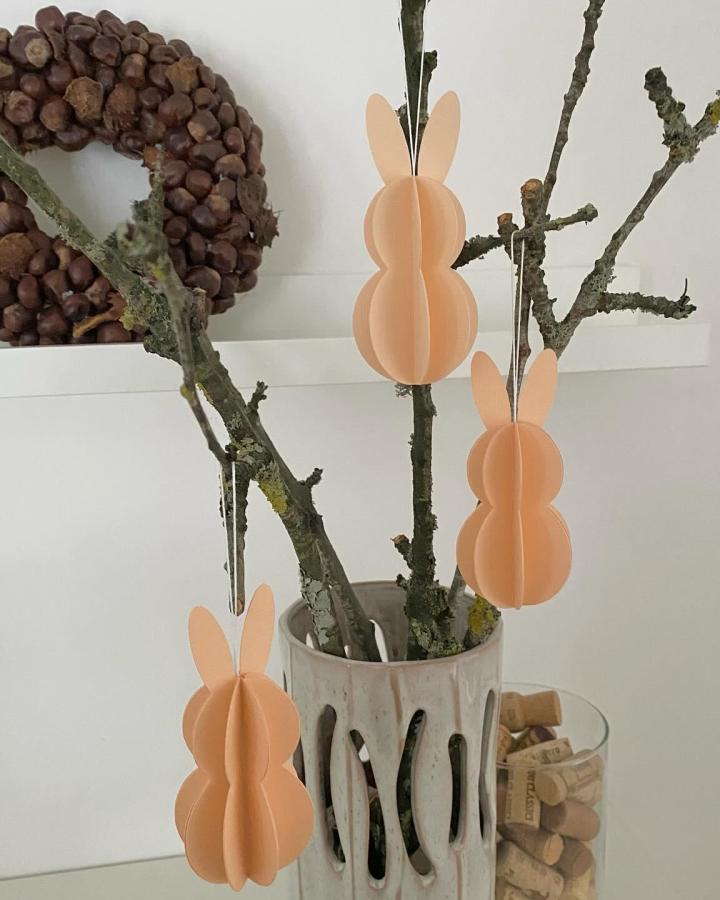 Peach paper bunny decorations hanging on twigs in a ceramic vase from @bymalamicraft simple elegant easter bunny crafts for adults.