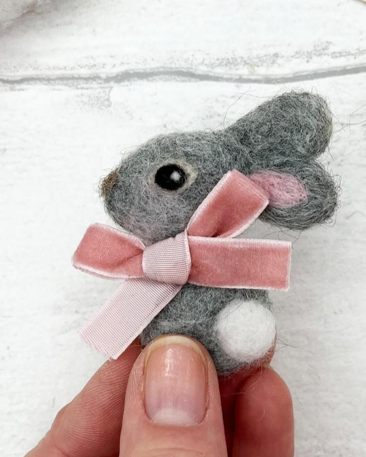 Grey felted bunny with a pink velvet bow held in fingers from @weareberginandbath, showcasing delicate easter bunny crafts for adults.