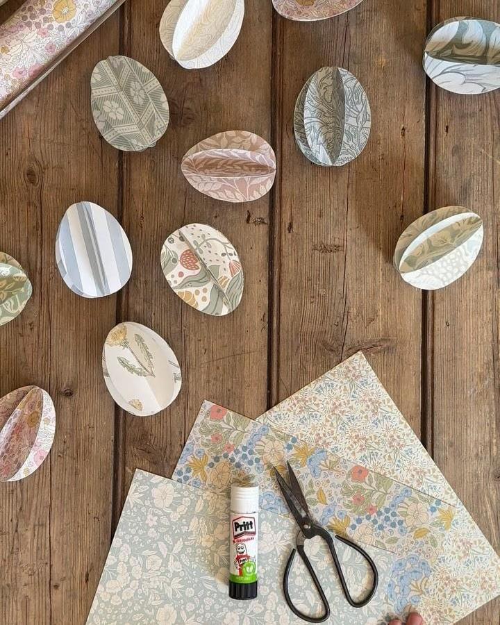 Soft pastel patterned paper 3D eggs on wooden surface with scissors and glue from @theottohouse for easter paper crafts for adults.