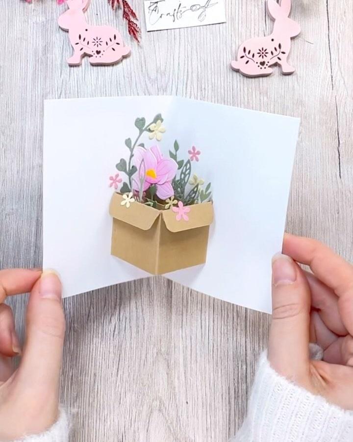 kraft paper pop up flower box card held by hands on wood table with pink bunny paper crafts easter paper crafts for adults