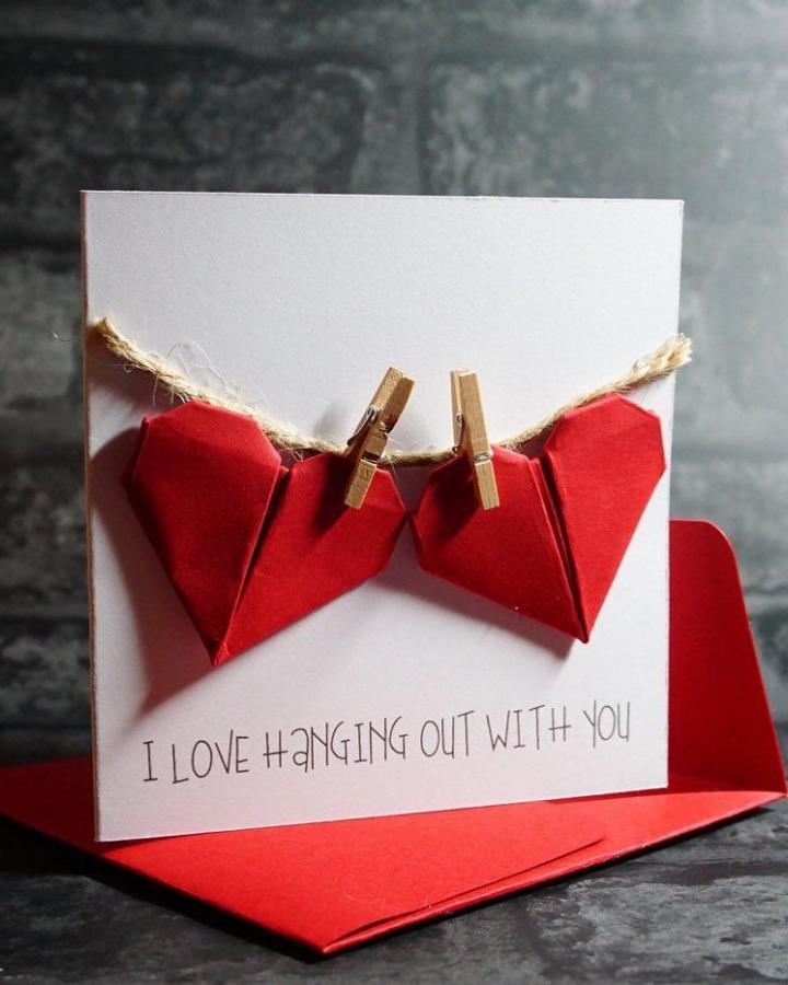 Red origami hearts clipped with mini wooden clothespins on twine string Valentine card handmade valentines card ideas from @the_makers_corner_uk. Rustic and playful craft design.