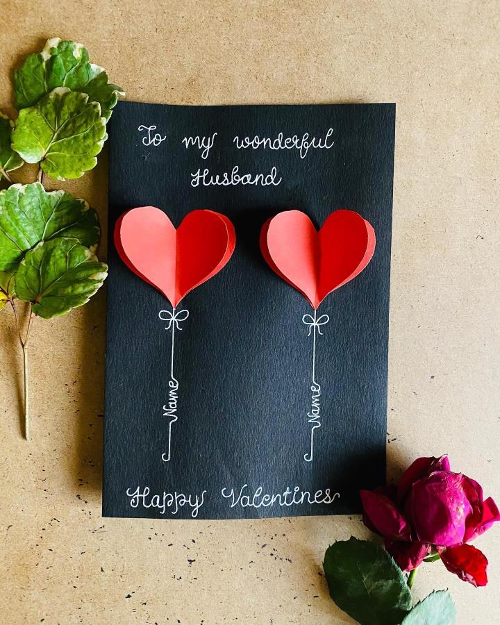 Black cardstock valentines card with 3D red and pink paper heart balloons from @thezentangleangle handmade valentines card ideas with white ink lettering and hand-drawn strings.